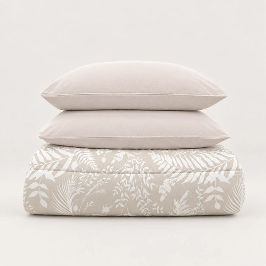 Couette d’hiver beige à motif de feuilles blanches, soigneusement pliée avec deux taies assorties.