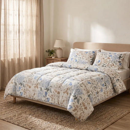 Cama de matrimonio vestida con un edredón estampado botánico en tonos azules y taupé, incluyendo dos fundas de almohada a juego en un dormitorio luminoso.