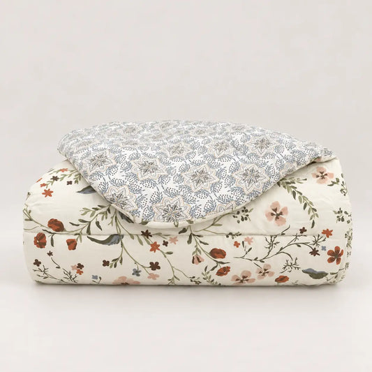 Couette de mi-saison soigneusement pliée, avec fleurs sauvages sur la face principale et motif géométrique au dos.