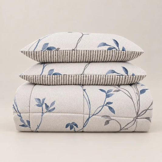 Couette d’hiver à motif floral bleu et dos à rayures, soigneusement pliée avec deux taies assorties.